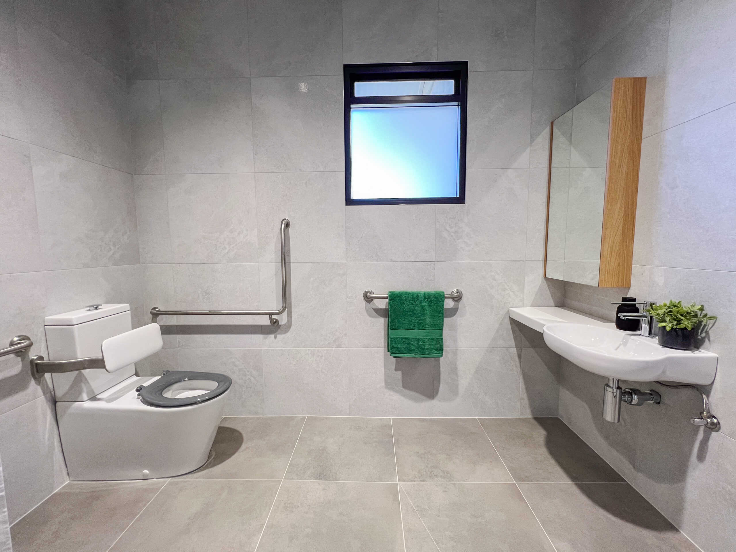 A wide view of the SDA bathroom, with the accessible toilet on the left and basin and vanity on the right. A green hand towel is hanging on the rack.